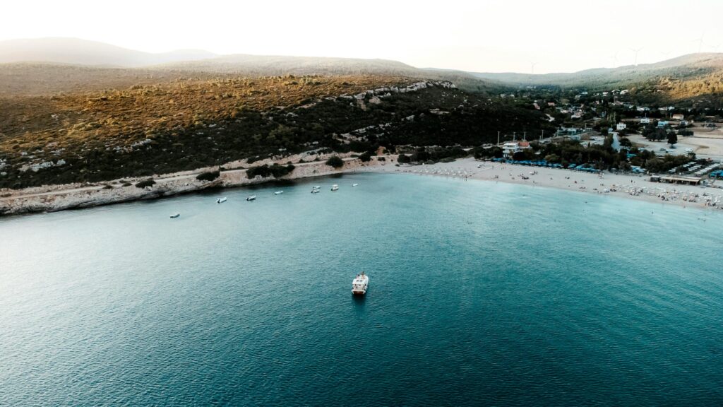 A stunning aerial photograph of a serene beach in Urla, Izmir, showcasing calm turquoise waters and lush hills.