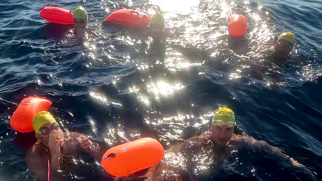 Swimmers receiving scheduled nutrition during the Bonifacio Strait crossing while remaining in the water alongside the escort boat.