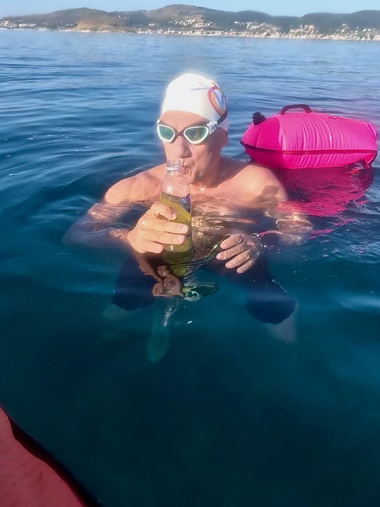 Open-water swimmer taking nutrition beside a support canoe during a Loop to Swim training session in Kaş.